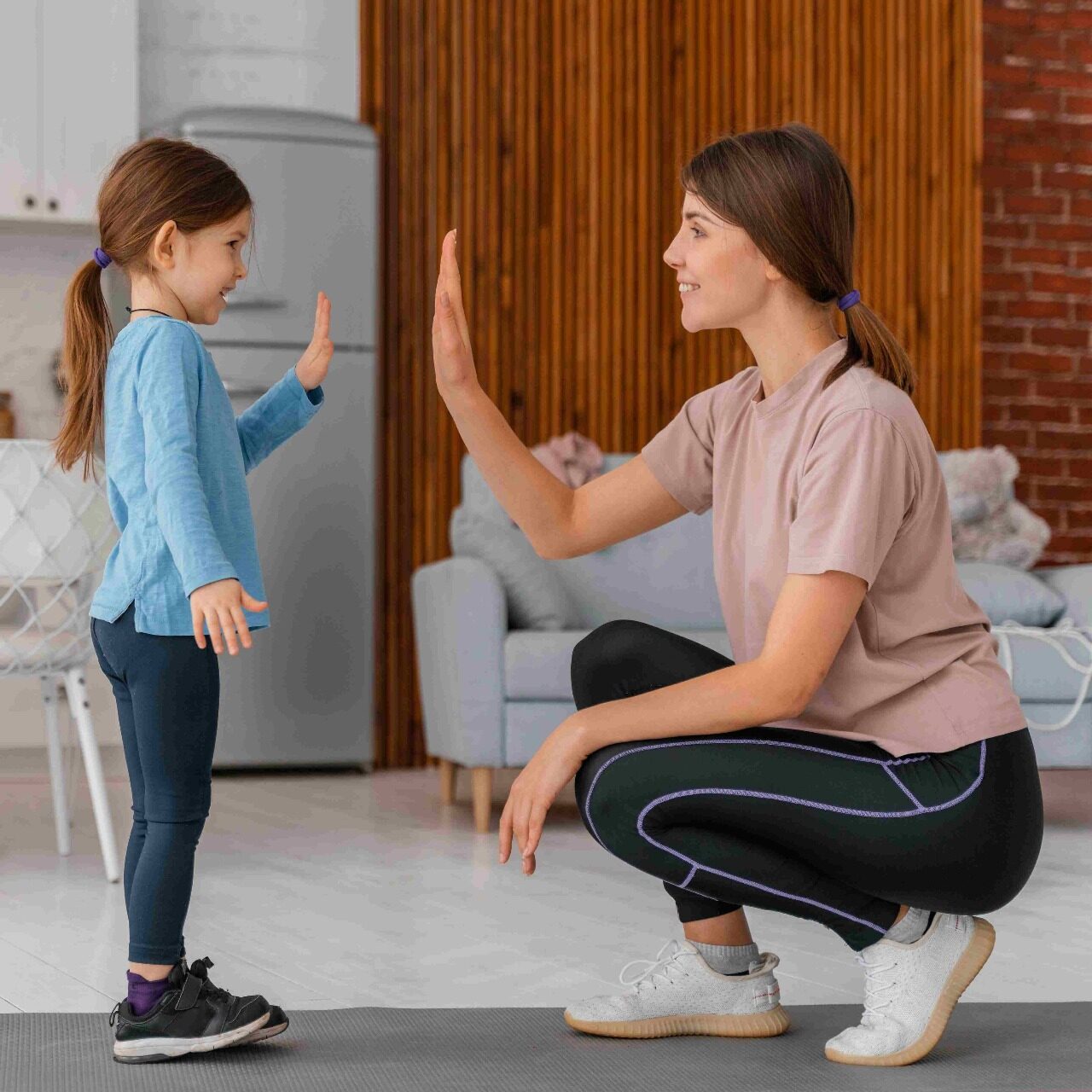 Mother and young daughter smiling and giving each other a high-five indoors during a playful bonding activity.